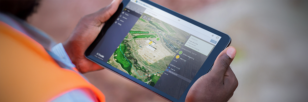 Worker holding a tablet in his hands, viewing Trimble site management software.