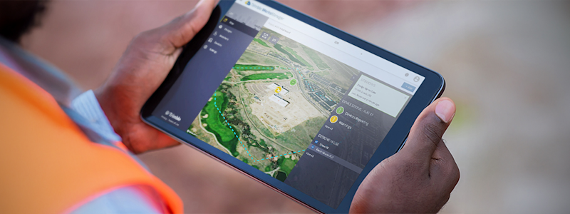 Worker holding a tablet in his hands, viewing Trimble site management software.