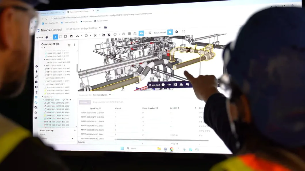 Two workers point at a complex 3D BIM piping model on a monitor using Trimble Connect2Fab software.