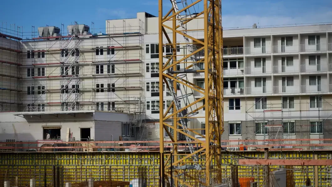 A yellow tower crane in front of a large multi-story building wrapped in scaffolding.