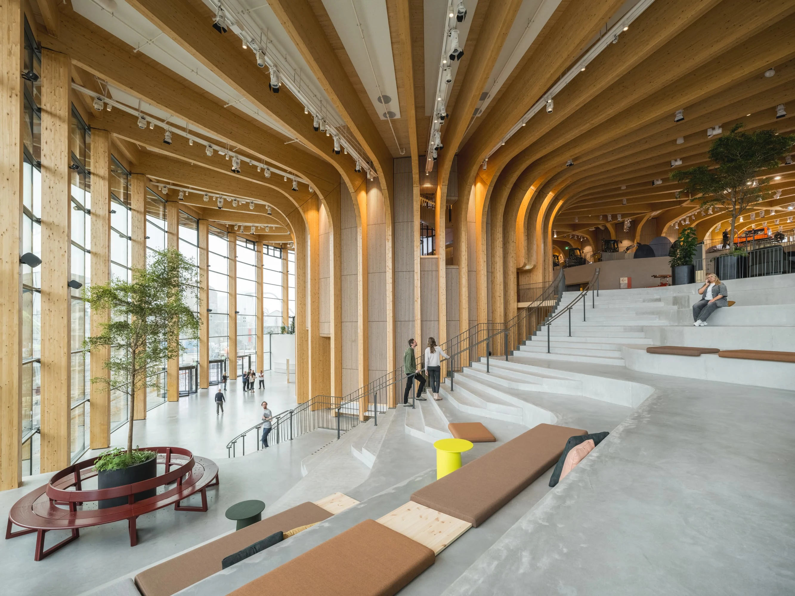 Interior view of the Grand Stairway at World of Volvo, featuring a dramatic curved wooden ceiling, tall windows and tiered concrete seating.