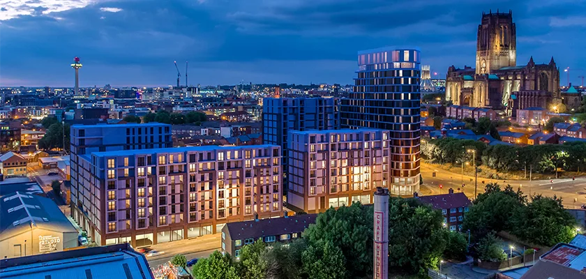 A wide aerial view of a modern city skyline at dusk, with contemporary residential buildings in the foreground and a large, historic cathedral.