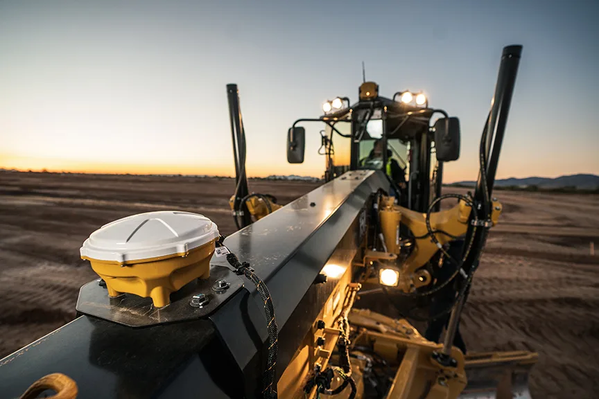 Yellow and white GPS receiver on a grader blade at sunset.