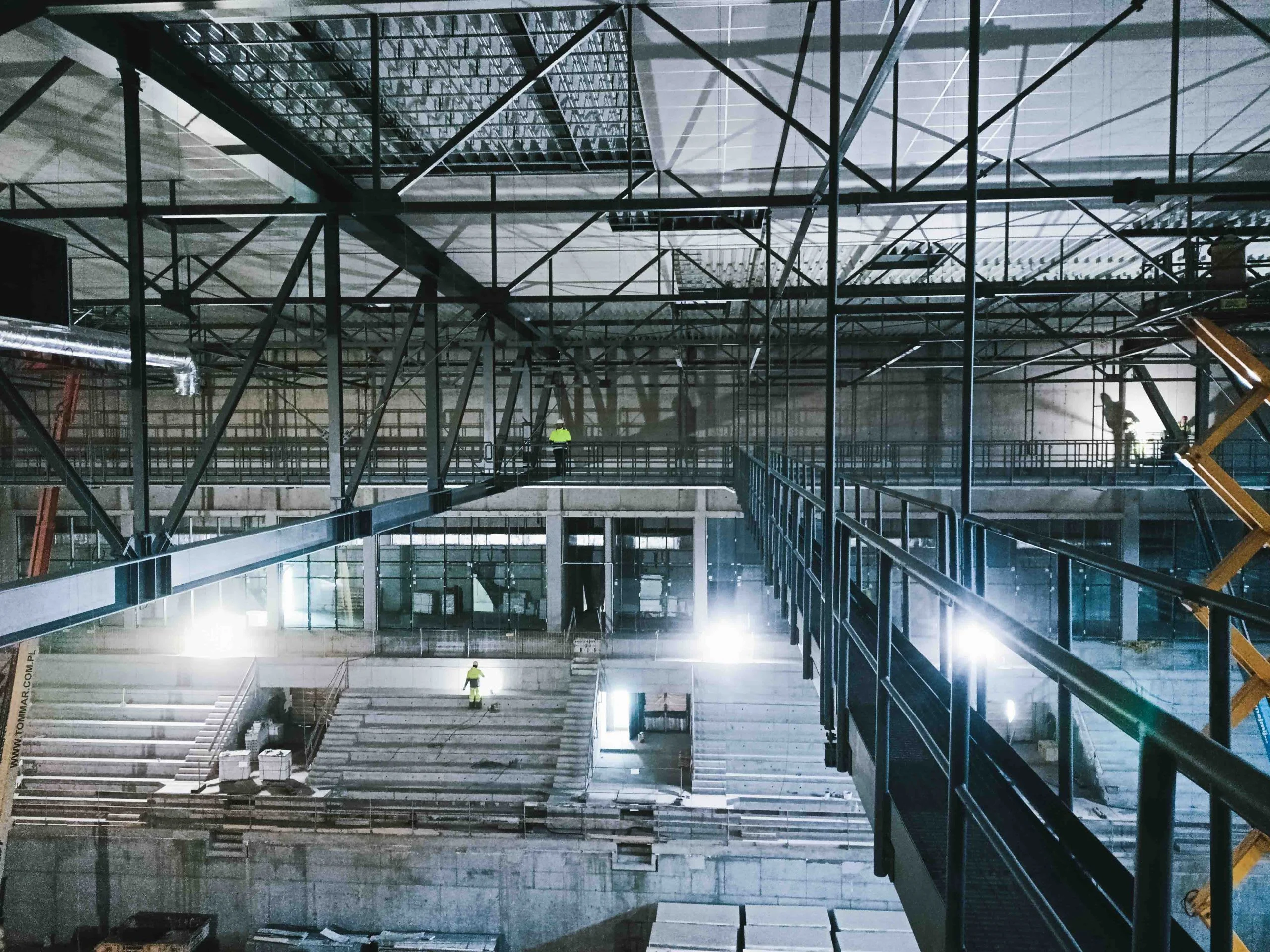 Construction of a large indoor sports arena with steel beams and unfinished concrete seating.