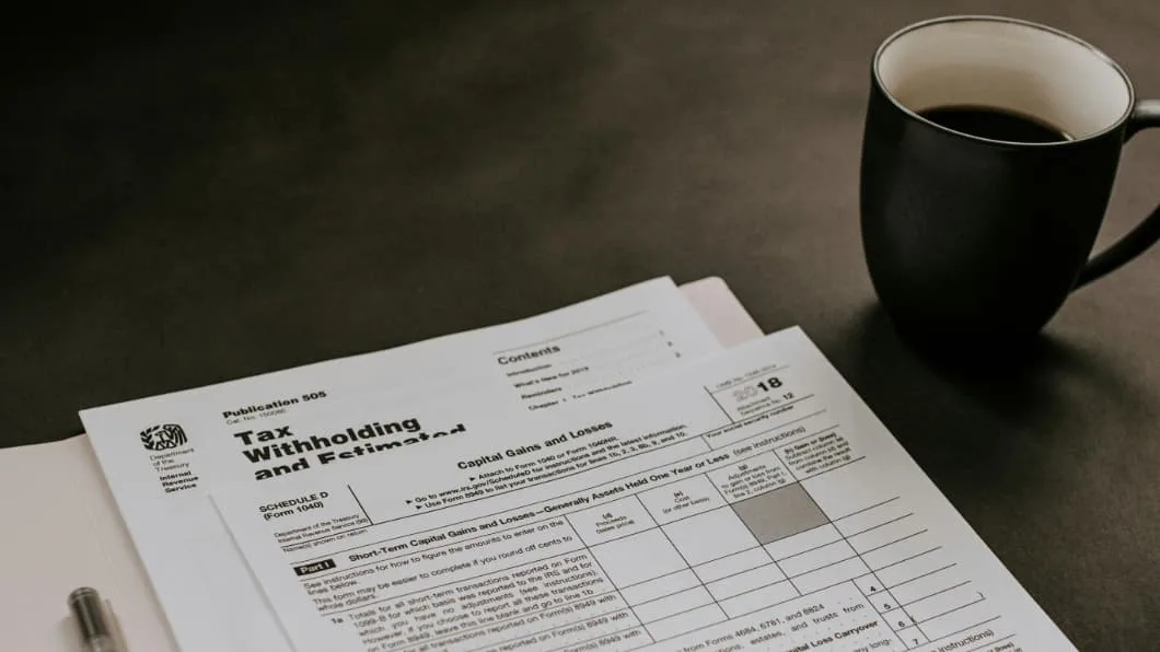 Close-up of IRS Publication 505 and Schedule D (Form 1040) for Capital Gains and Losses with a pen and coffee.