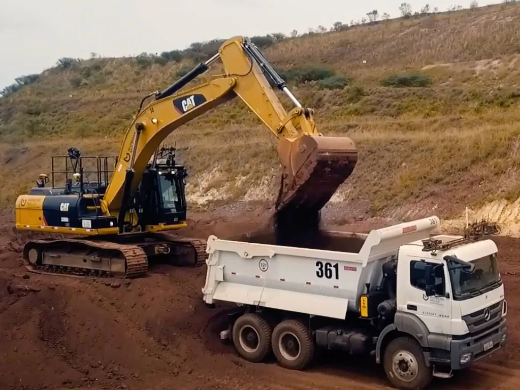 A yellow excavator dumps dirt into a white dump truck at a construction site.