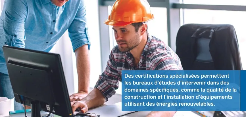 Two male construction professionals, one wearing an orange hard hat, look at a computer screen.