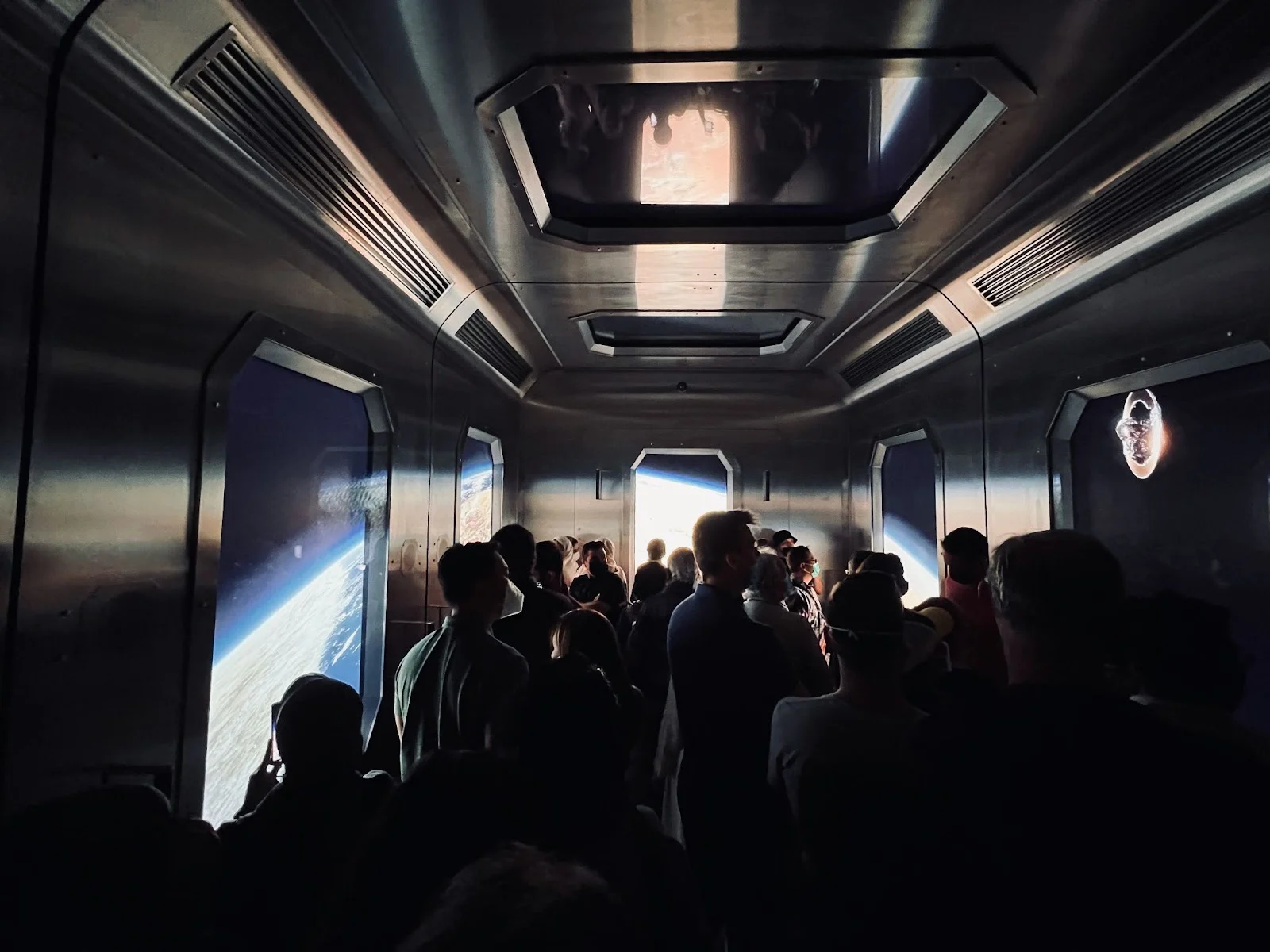 People gathered in a futuristic hallway with projections of Earth and space.