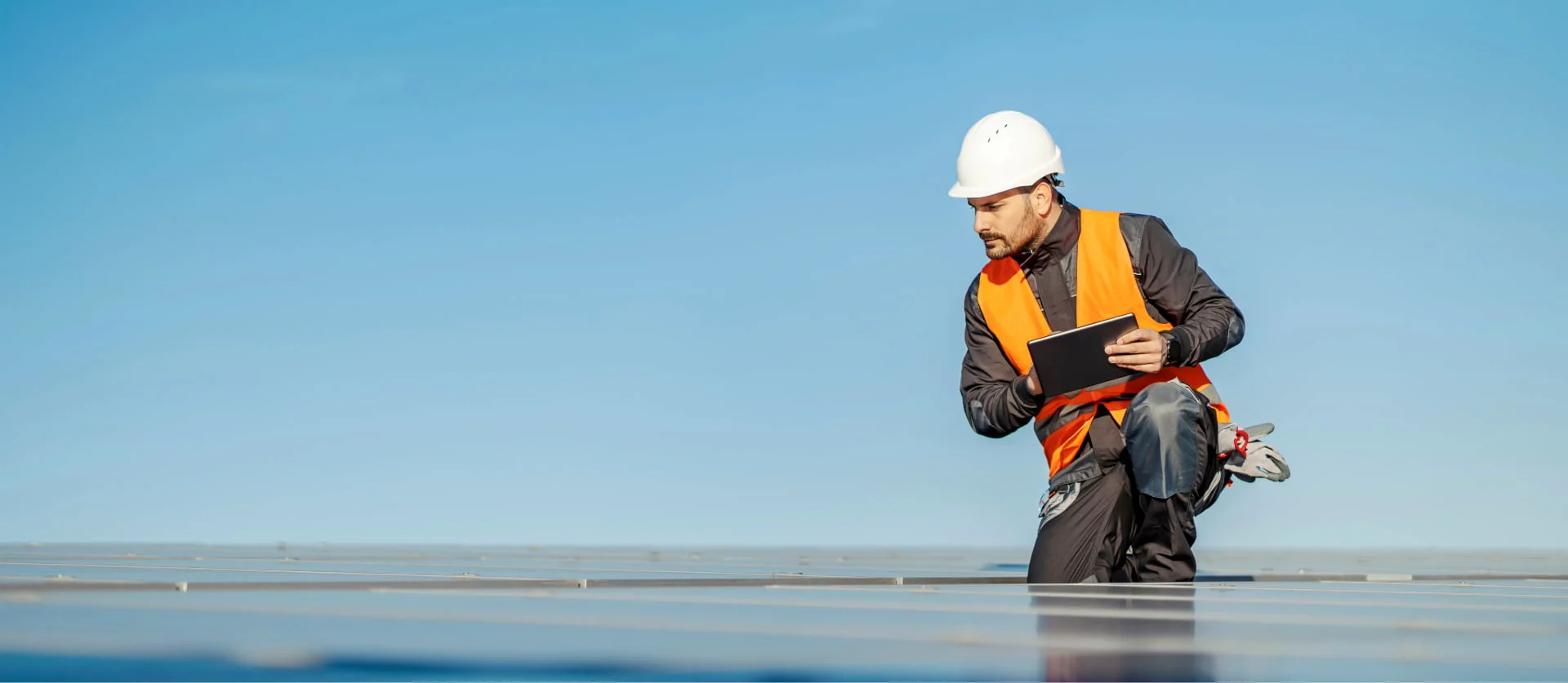 Technicus in veiligheidsvest gebruikt een tablet op een dak met zonnepanelen.