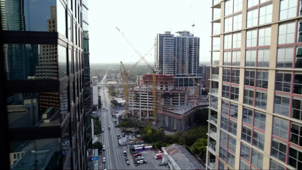 Cityscape with skyscrapers and construction cranes under a cloudy sky.