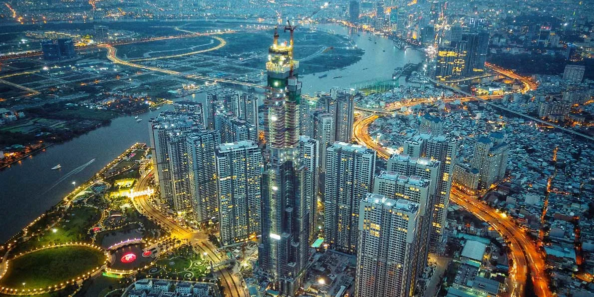An aerial view of a city skyline at night, with a river running through it, illuminated by the lights of buildings and roads.