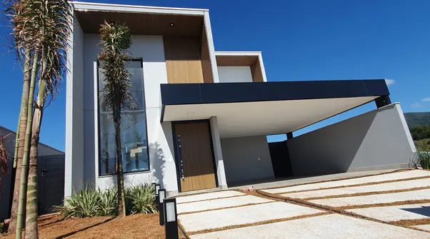 A modern gray two-story house with a black overhang, a wooden door, and a tall narrow window.