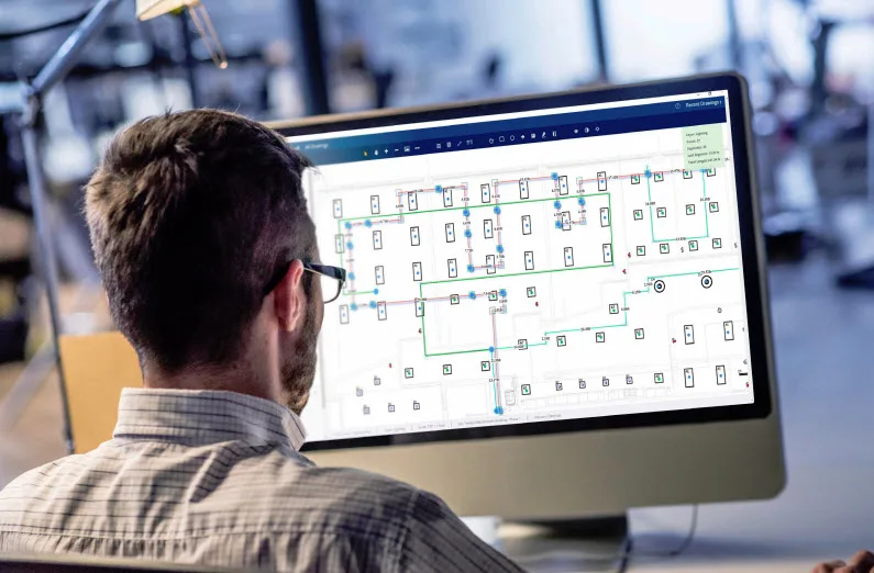 Man in glasses reviews a complex building electrical diagram on a computer screen.