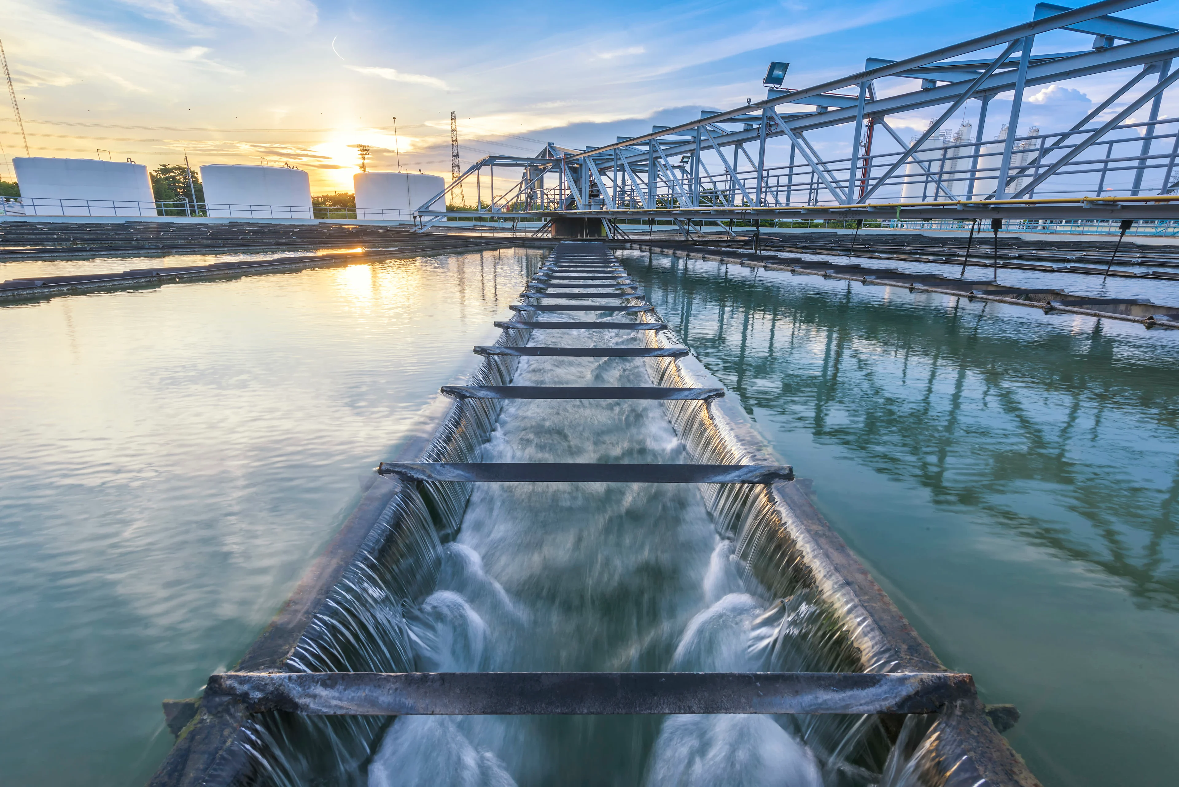Water treatment facility with cascading water flow and industrial infrastructure under a sunset sky.