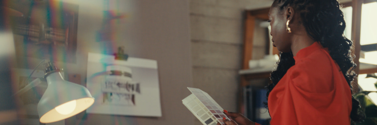 Tola holds colour swatches whilst observing designs pinned to the wall in her workspace.