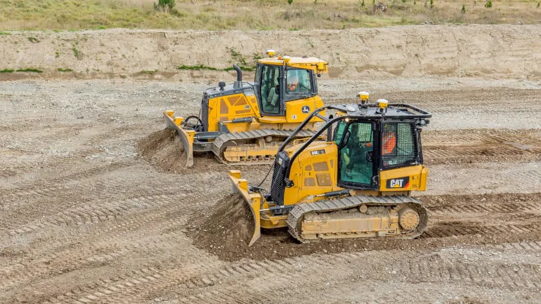 Two heavy-duty bulldozers, a John Deere and a CAT, grading earth at a construction site.