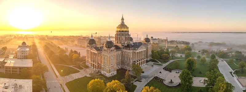 The Iowa State Capitol at sunrise, its Renaissance sandstone and brick architecture, featuring a gold-leaf central dome and four other domes, emerges from fog.