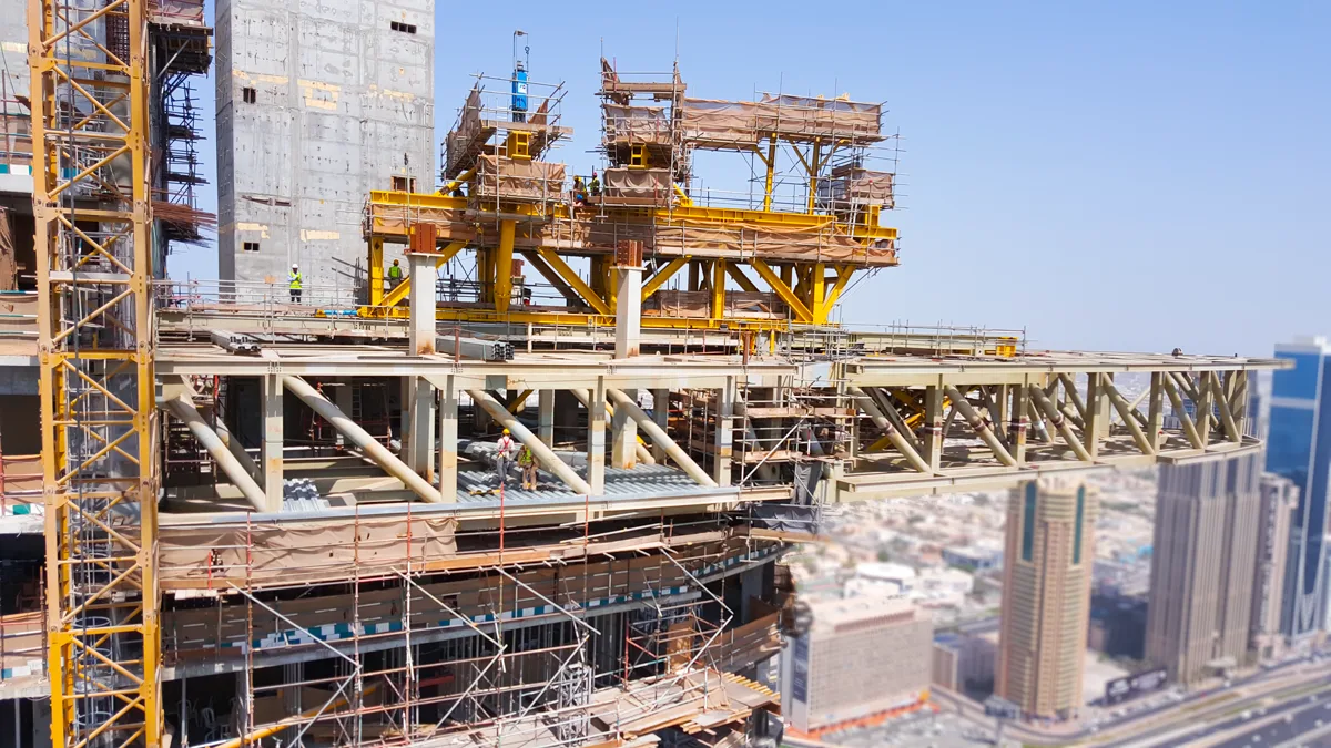A large construction project is underway, with workers and yellow cranes visible on a high-rise building.
