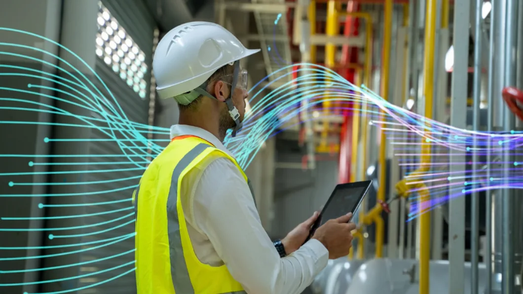 Engineer in safety gear using a tablet to inspect industrial equipment.