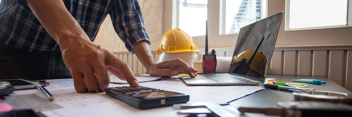 Construction HR team member at desk with pens, papers, post it notes and calculator to handle complex HR processes.
