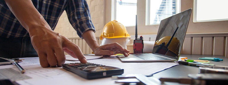 Construction HR team member at desk with pens, papers, post it notes and calculator to handle complex HR processes.