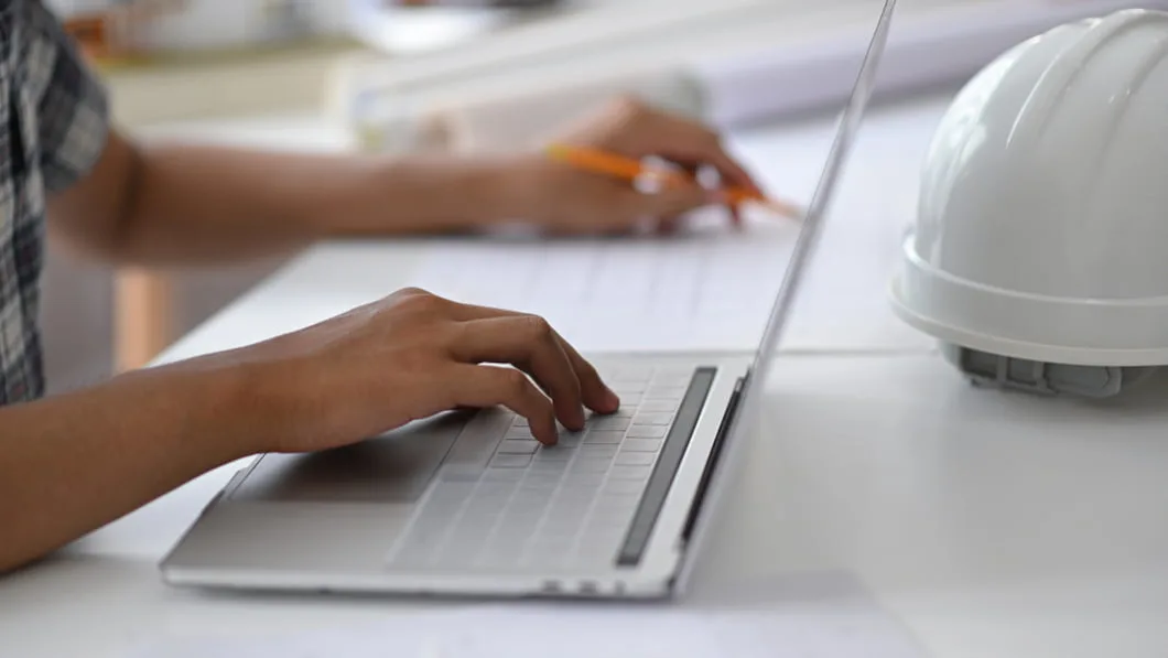 Construction HR team member using laptop to enter all information into one modern HR portal for construction industry.