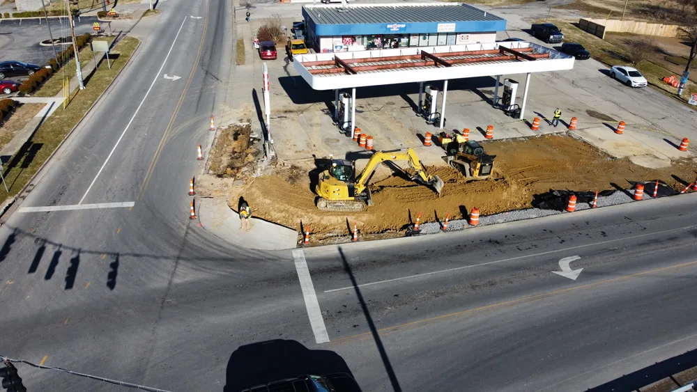 Excavators and orange cones are on site at a gas station undergoing road construction.