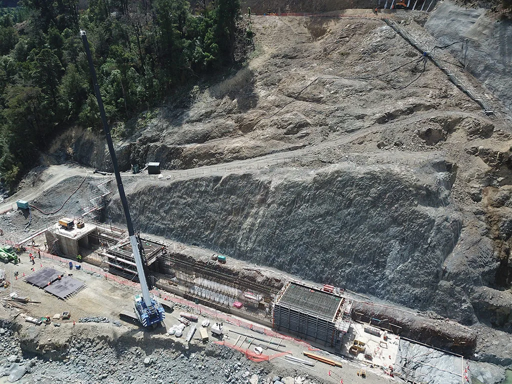 Construction site with a large crane and concrete structures being built into a rocky hillside.