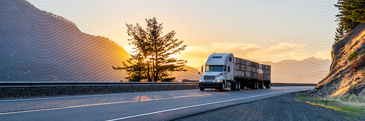 Semi-truck driving on a scenic highway at sunset, with mountains and trees in the background.