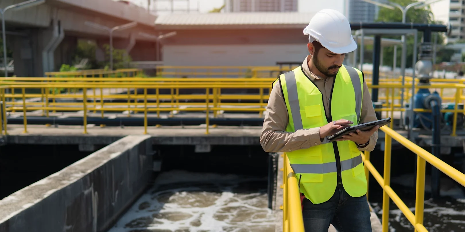 Engineer in safety gear using a tablet at a water treatment facility.