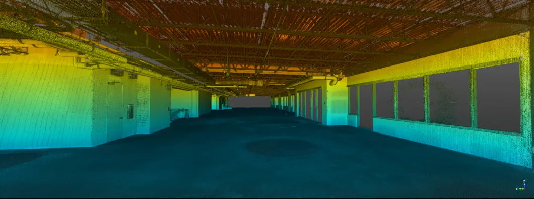 Empty industrial space with colorful gradient lighting in blue, green, and yellow illuminating the walls and exposed ceiling.