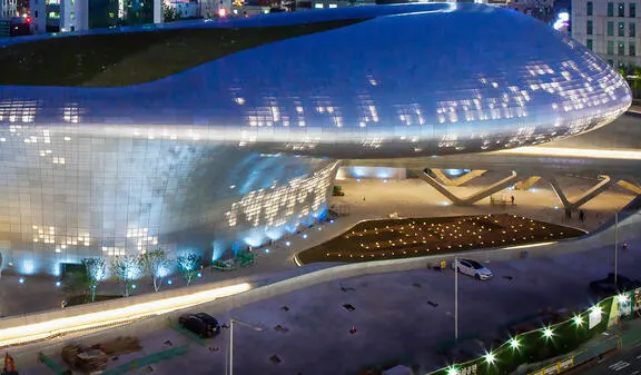 A futuristic building with a metallic, curved facade illuminated at night, with small lights scattered across its surface and along its base.