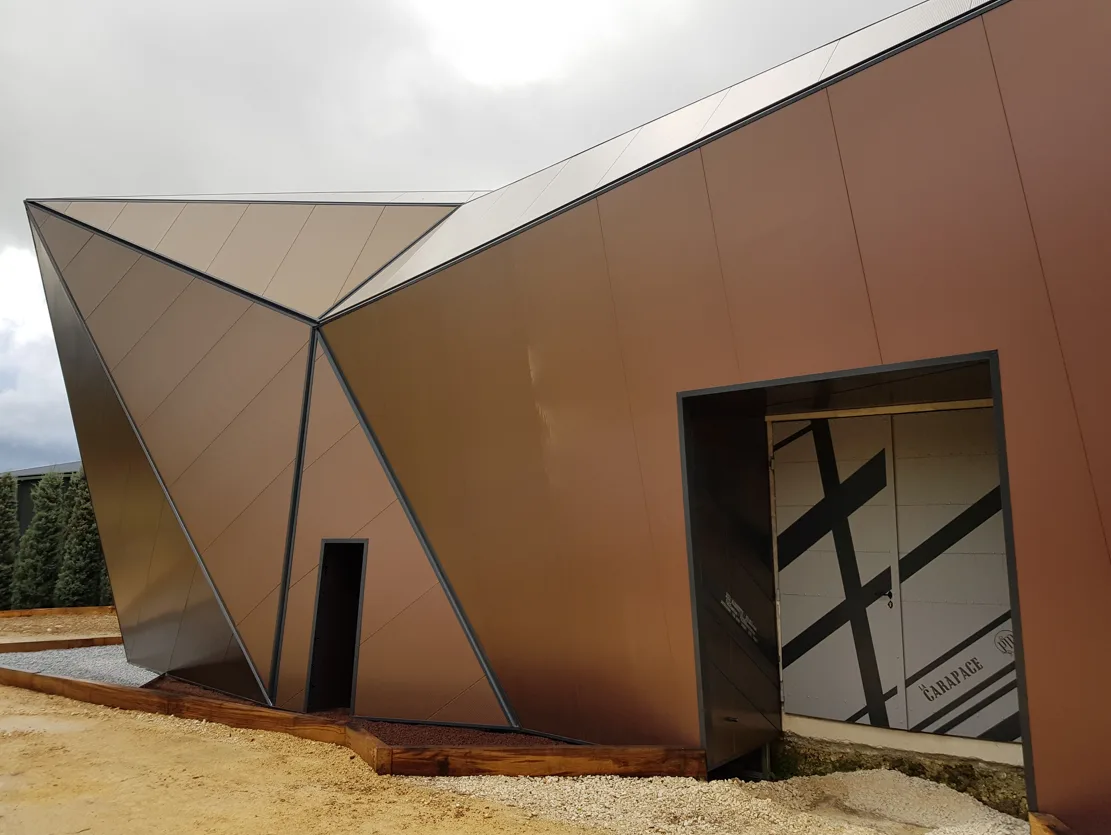 The exterior of a modern building with angular, bronze-colored panels and a dark doorway.