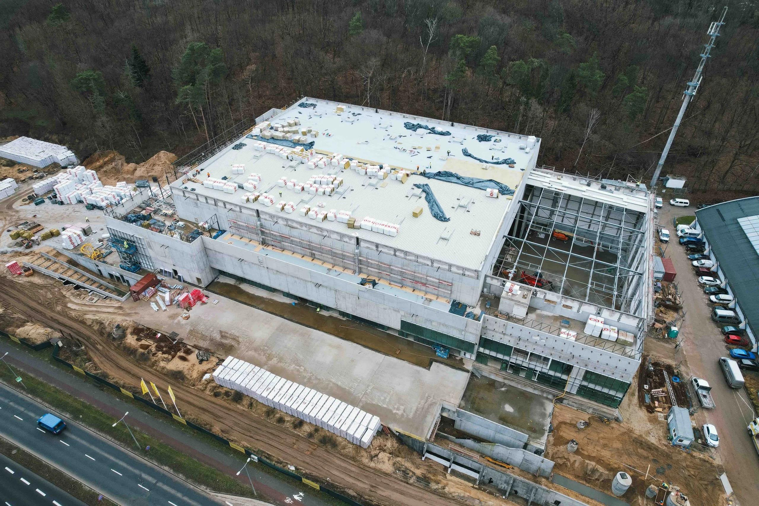 Aerial view of a large industrial building under construction, with exposed steel framework and concrete walls.
