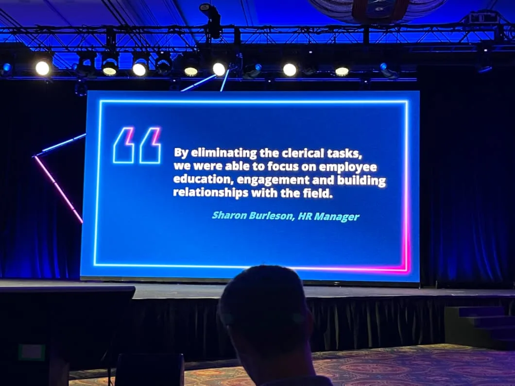 A stage screen displays an HR manager's quote on focusing on employee education and engagement by eliminating clerical tasks. Conference setting.