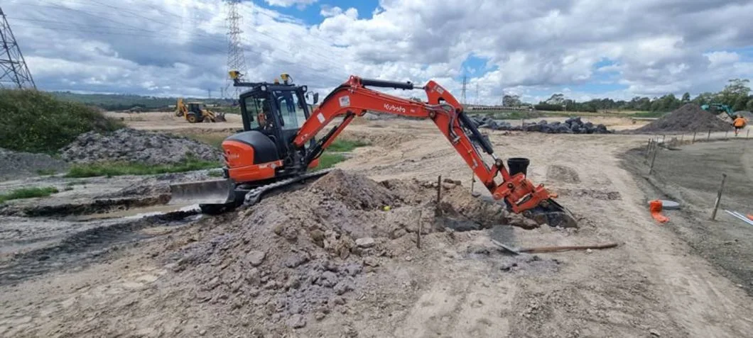 Orange excavator working on a construction site under a cloudy sky.