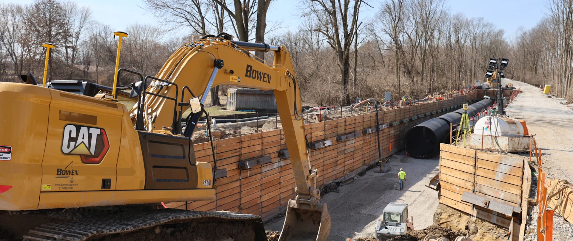 A Caterpillar bulldozer with the Bowen brand excavates debris on the side of a country road.