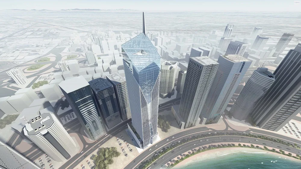 Aerial view of a modern city centered on a glass skyscraper with a faceted top, surrounded by other buildings, a coastal road, and the sea.