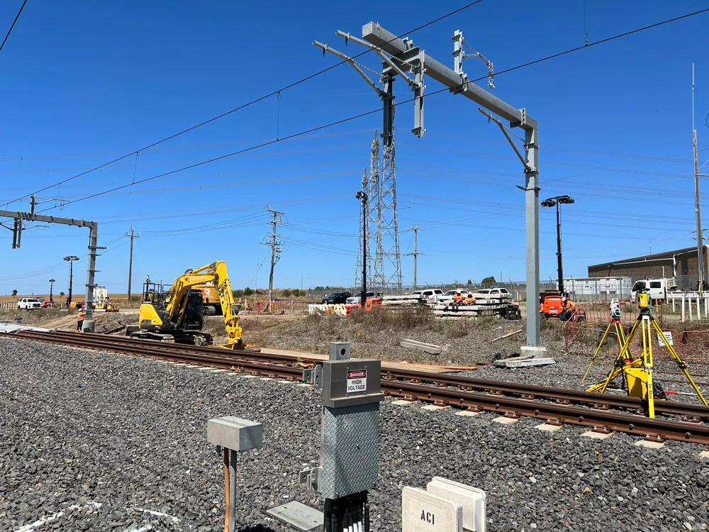 Construction site with train tracks, an excavator, overhead lines and surveying equipment.