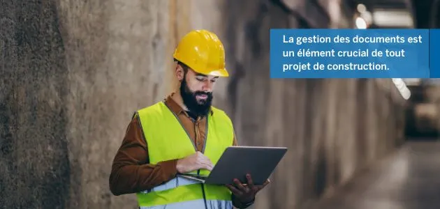 A construction worker wearing a hard hat and safety vest looks at a laptop in a tunnel.