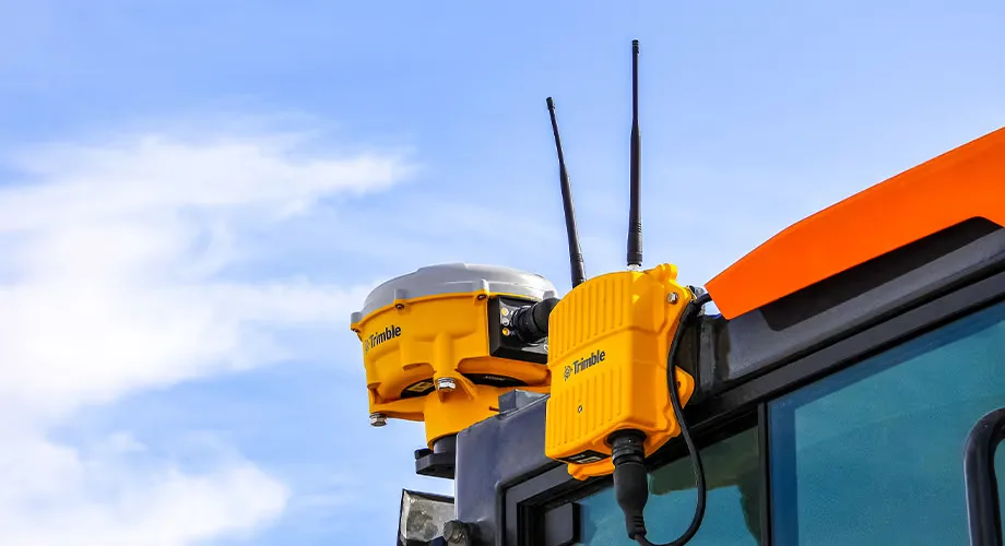 Close-up of a Trimble GPS receiver and communications device mounted on construction equipment under a blue sky.
