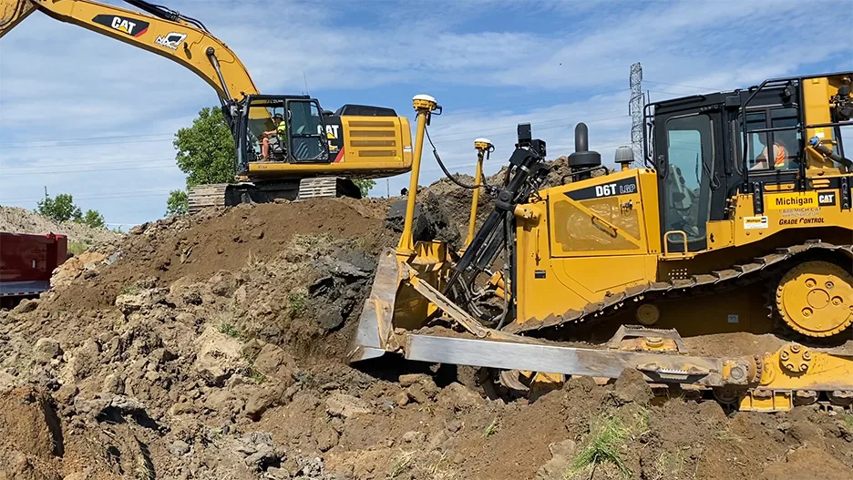 A yellow bulldozer pushes dirt, with a yellow excavator in the background at a construction site.