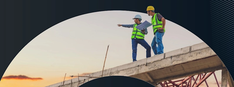 Two construction workers in yellow vests and hard hats review blueprints atop a concrete structure at sunset.