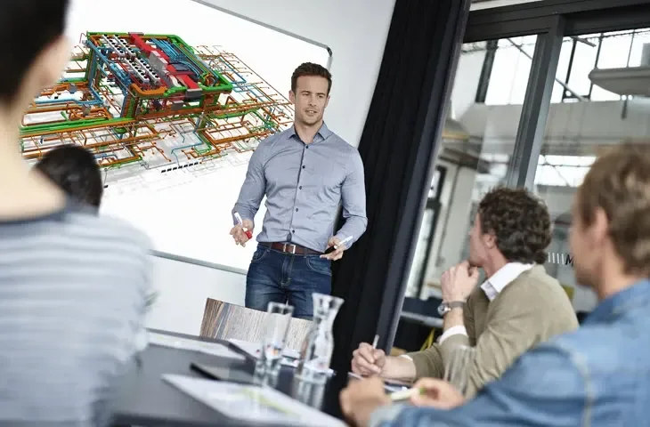 A presenter stands in front of a whiteboard displaying a 3D BIM model, while an audience watches.