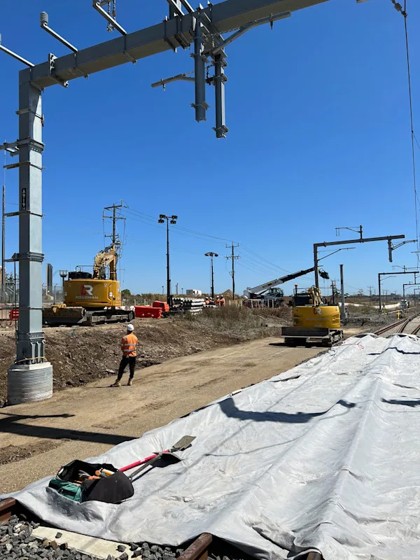 Construction of new overhead electrical lines for a railway with excavators and a worker on-site.