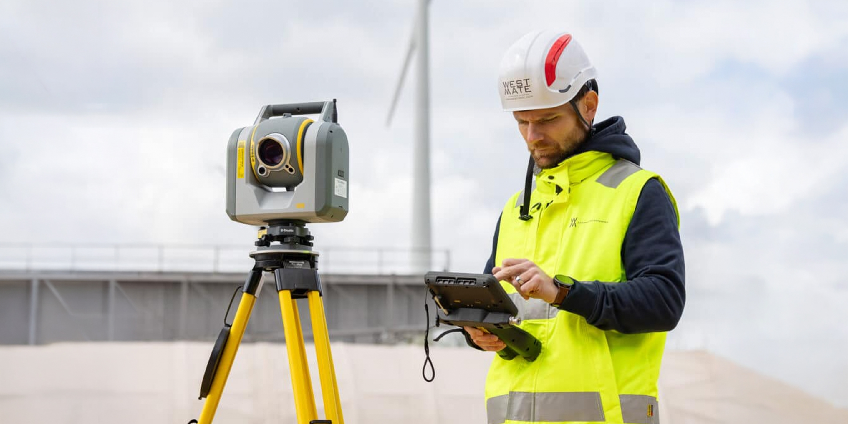 Man with a controller stands next to a total station on a bridge project.