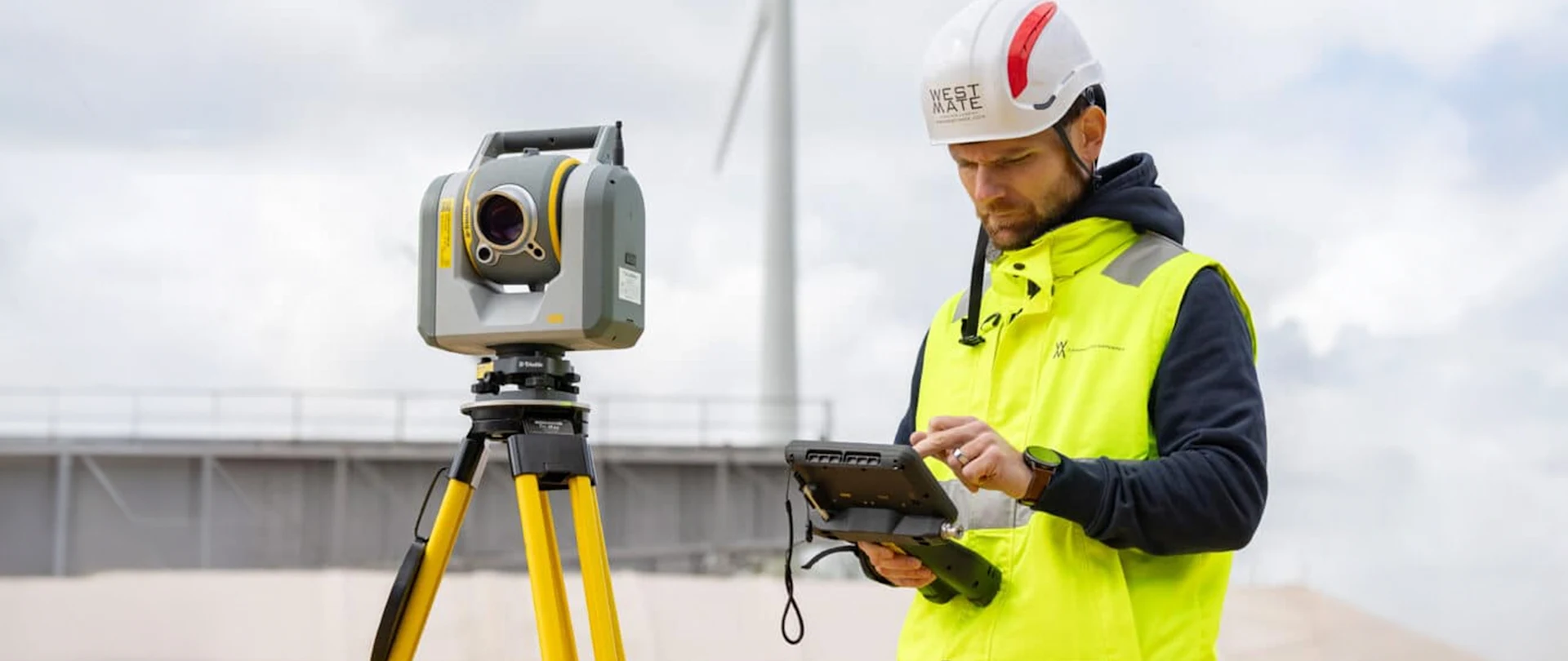 Man with a controller stands next to a total station on a bridge project.