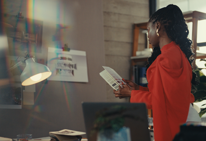 Tola holds colour swatches whilst observing designs pinned to the wall in her workspace.