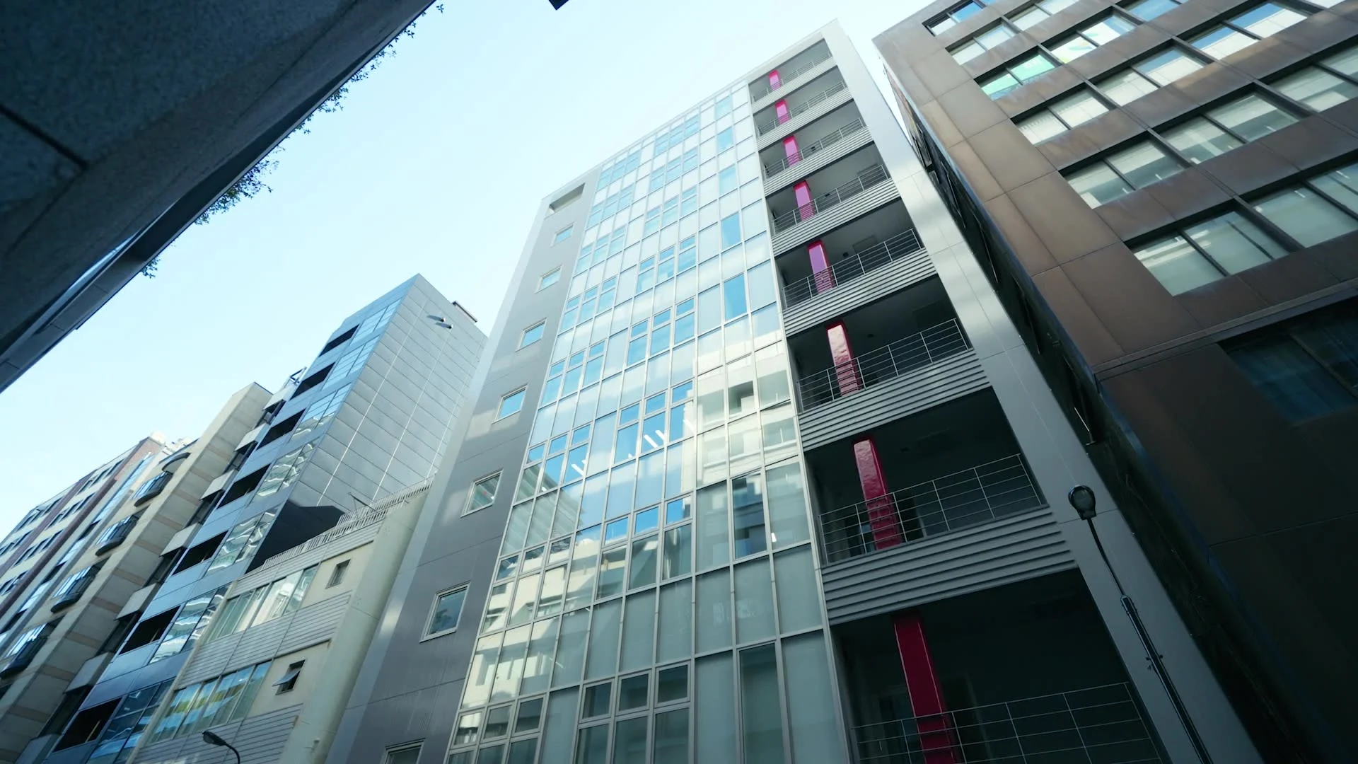 Looking up at a row of modern office buildings with glass facades against a clear blue sky.