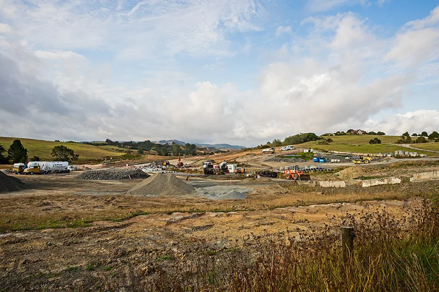 Construction site with piles of gravel and various heavy machinery under a cloudy sky.